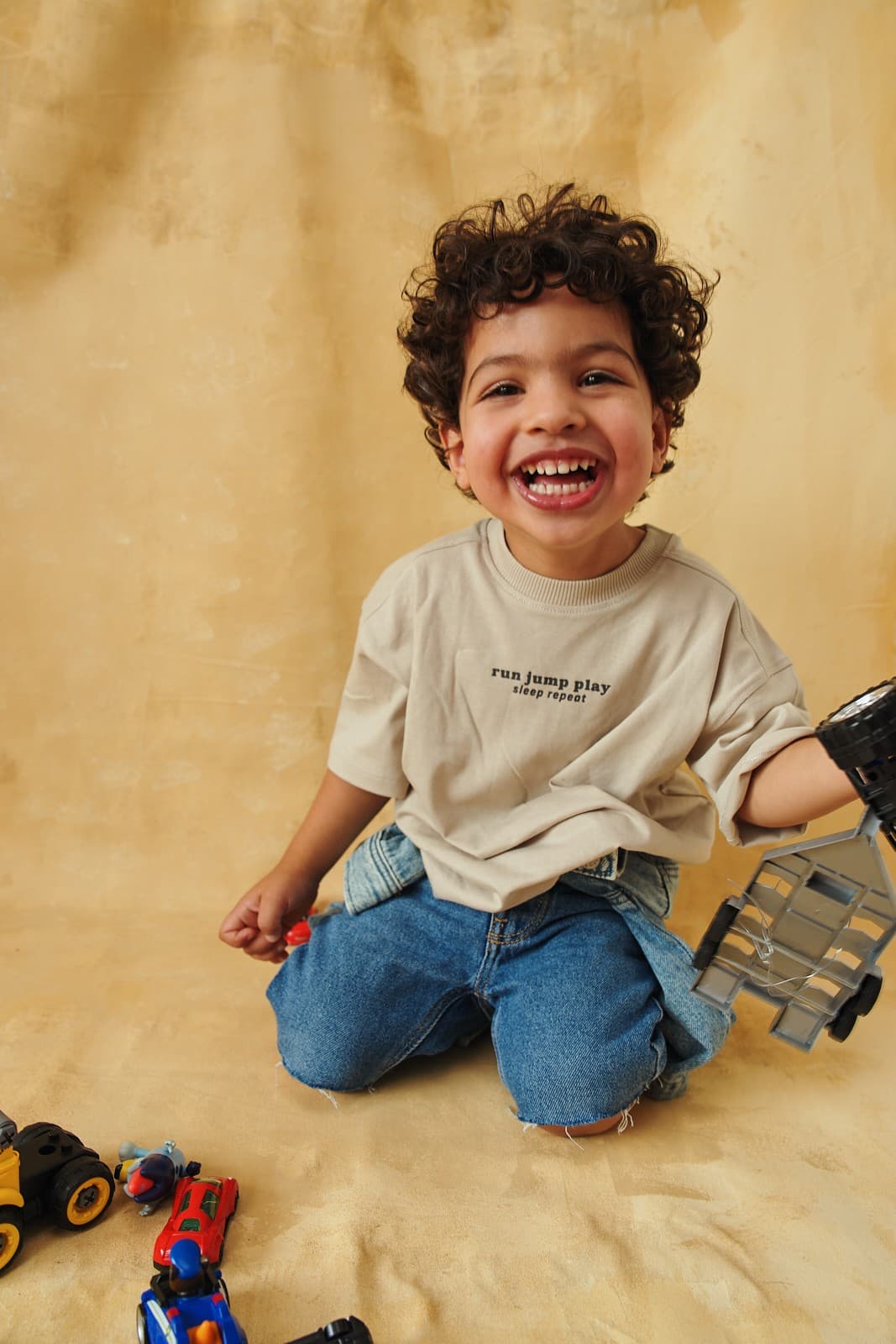 Studio lifestyle campaign of a toddler laughing while playing with toy cars on a warm ochre backdrop in Vancouver by Una Zhu
